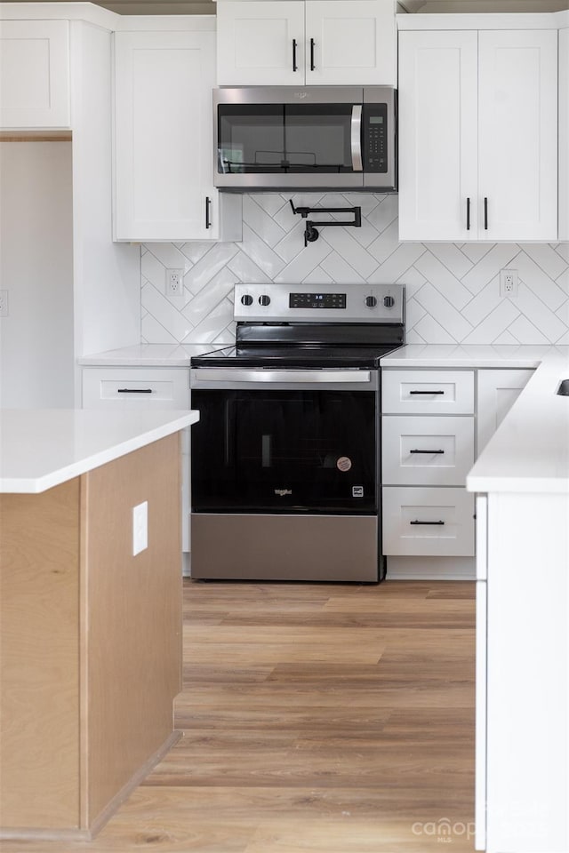 kitchen with stainless steel appliances, light countertops, light wood-style floors, white cabinetry, and backsplash