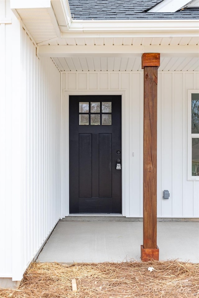 view of exterior entry with board and batten siding and roof with shingles