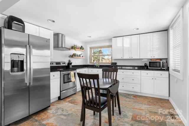 kitchen featuring appliances with stainless steel finishes, white cabinetry, wall chimney range hood, and sink