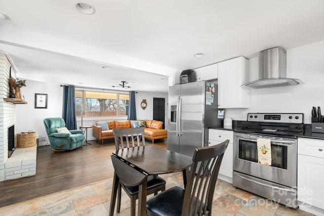 kitchen featuring stainless steel appliances, white cabinets, a brick fireplace, and wall chimney exhaust hood