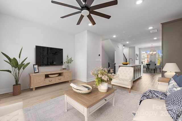 living room featuring light hardwood / wood-style floors, sink, and ceiling fan with notable chandelier