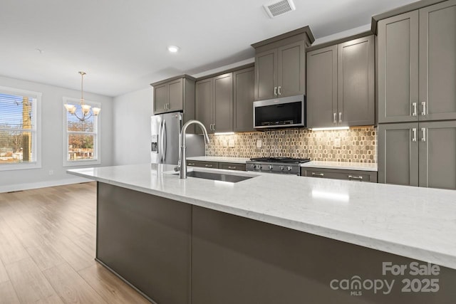 kitchen featuring stainless steel appliances, a notable chandelier, hanging light fixtures, light stone counters, and sink