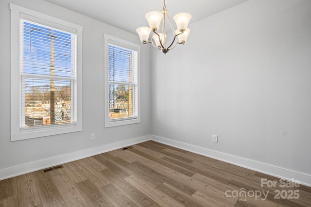 empty room featuring a wealth of natural light, an inviting chandelier, and hardwood / wood-style floors