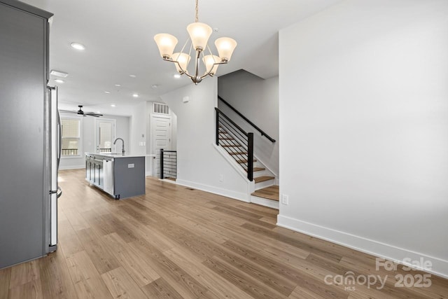 living room with ceiling fan with notable chandelier, light hardwood / wood-style flooring, and sink