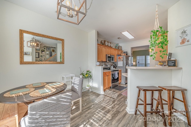 kitchen featuring kitchen peninsula, appliances with stainless steel finishes, a kitchen breakfast bar, a chandelier, and light hardwood / wood-style floors