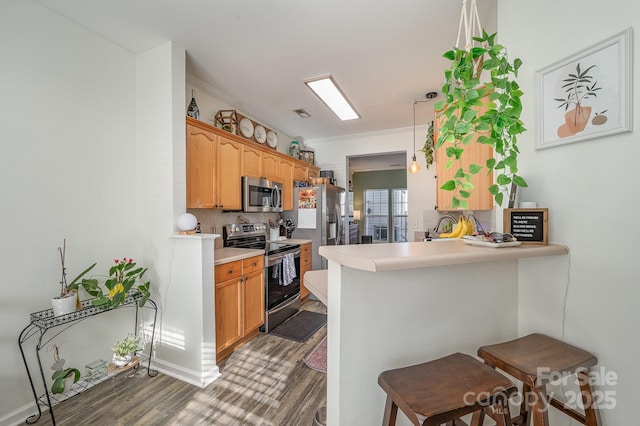 kitchen with pendant lighting, dark wood-type flooring, appliances with stainless steel finishes, kitchen peninsula, and a breakfast bar area