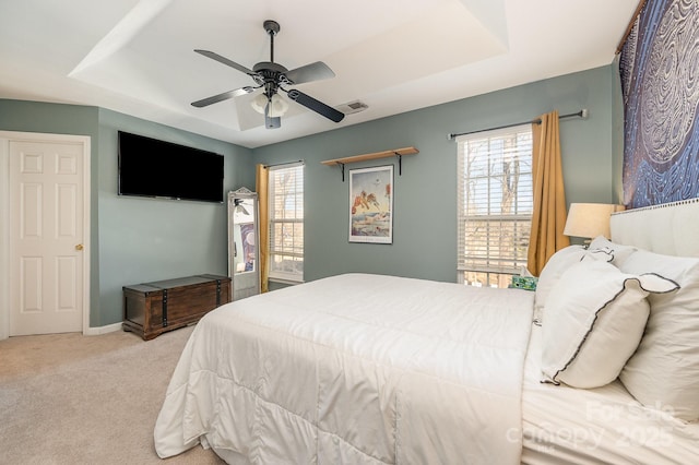 bedroom with a raised ceiling, multiple windows, ceiling fan, and light colored carpet