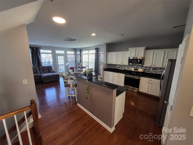 kitchen featuring appliances with stainless steel finishes, backsplash, white cabinets, a kitchen bar, and plenty of natural light