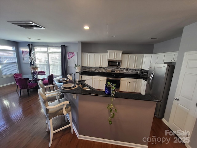 kitchen featuring a breakfast bar, appliances with stainless steel finishes, hanging light fixtures, white cabinets, and a center island with sink