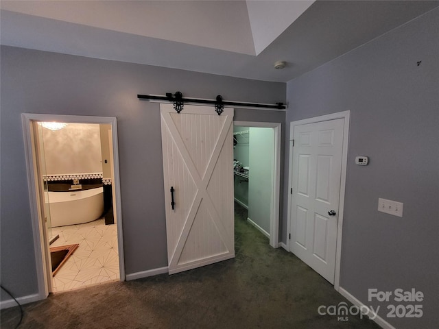 unfurnished bedroom with ensuite bath, a spacious closet, a barn door, dark carpet, and a closet