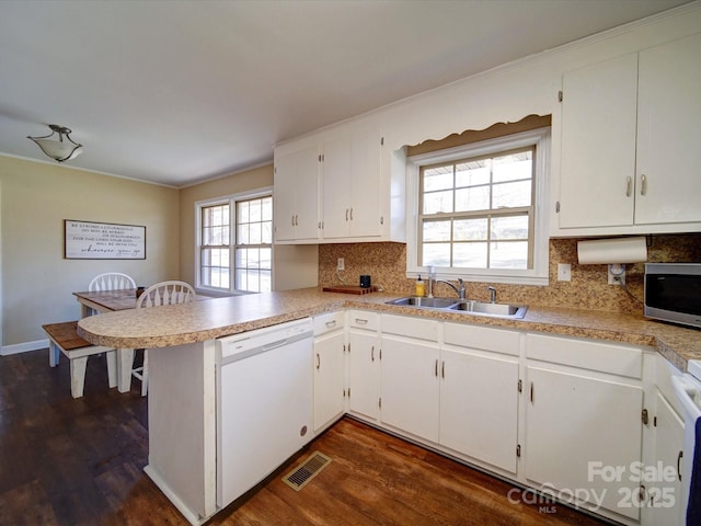 kitchen with white dishwasher, kitchen peninsula, sink, tasteful backsplash, and white cabinetry