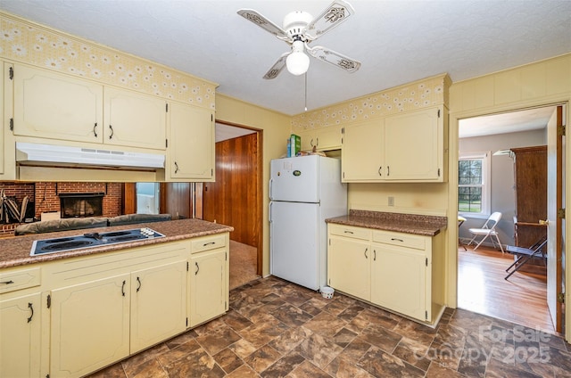 kitchen featuring ceiling fan, stovetop, white fridge, and cream cabinetry