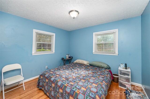 bedroom featuring multiple windows, light hardwood / wood-style flooring, and a textured ceiling