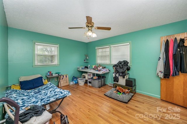 bedroom featuring multiple windows, a textured ceiling, light hardwood / wood-style floors, and ceiling fan