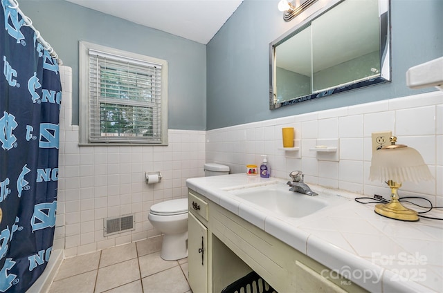 bathroom featuring walk in shower, tile patterned flooring, toilet, vanity, and tile walls