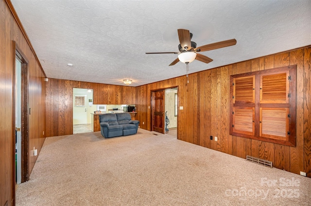 unfurnished living room featuring a textured ceiling, carpet floors, ceiling fan, and wood walls