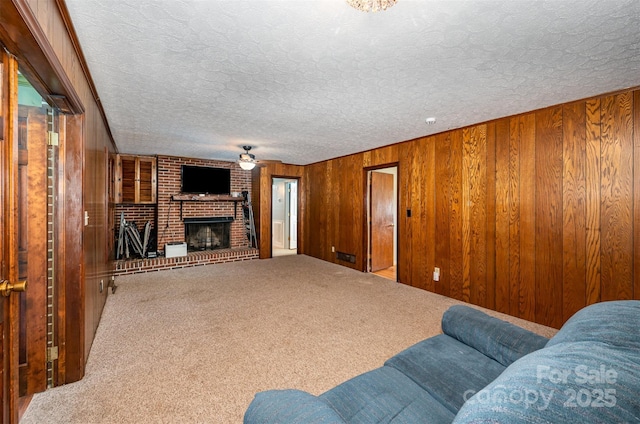 carpeted living room with a textured ceiling, wood walls, and a fireplace