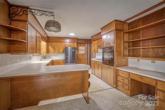 kitchen with kitchen peninsula, stainless steel fridge, a textured ceiling, sink, and black oven