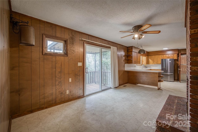 kitchen featuring wood walls, sink, ceiling fan, kitchen peninsula, and stainless steel refrigerator