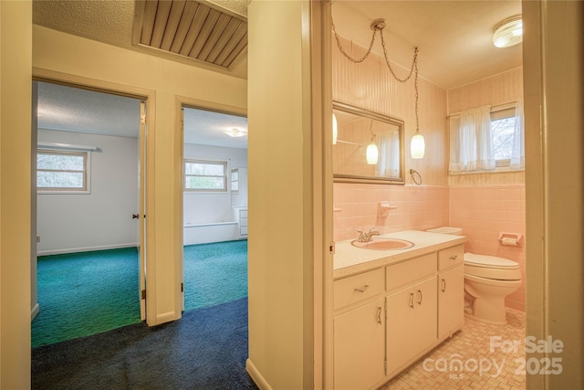 bathroom with a textured ceiling, vanity, tile walls, and a wealth of natural light