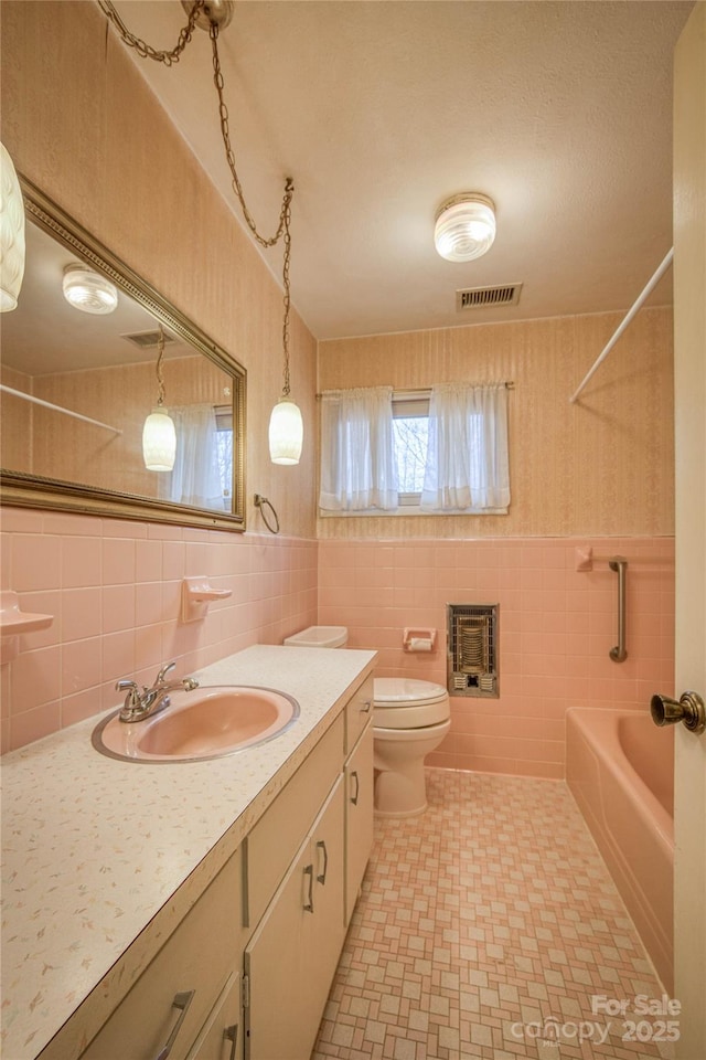 bathroom with heating unit, vanity, tile walls, and toilet