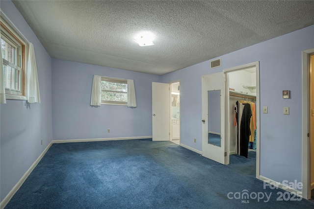 unfurnished bedroom with a spacious closet, a closet, dark carpet, and a textured ceiling