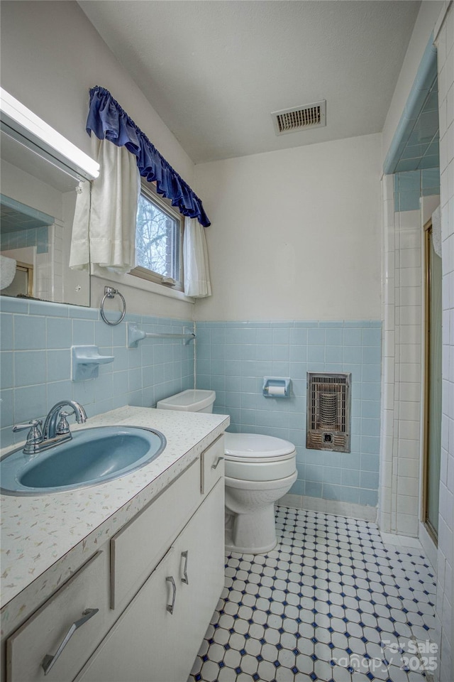 bathroom with tile patterned flooring, heating unit, an enclosed shower, vanity, and tile walls