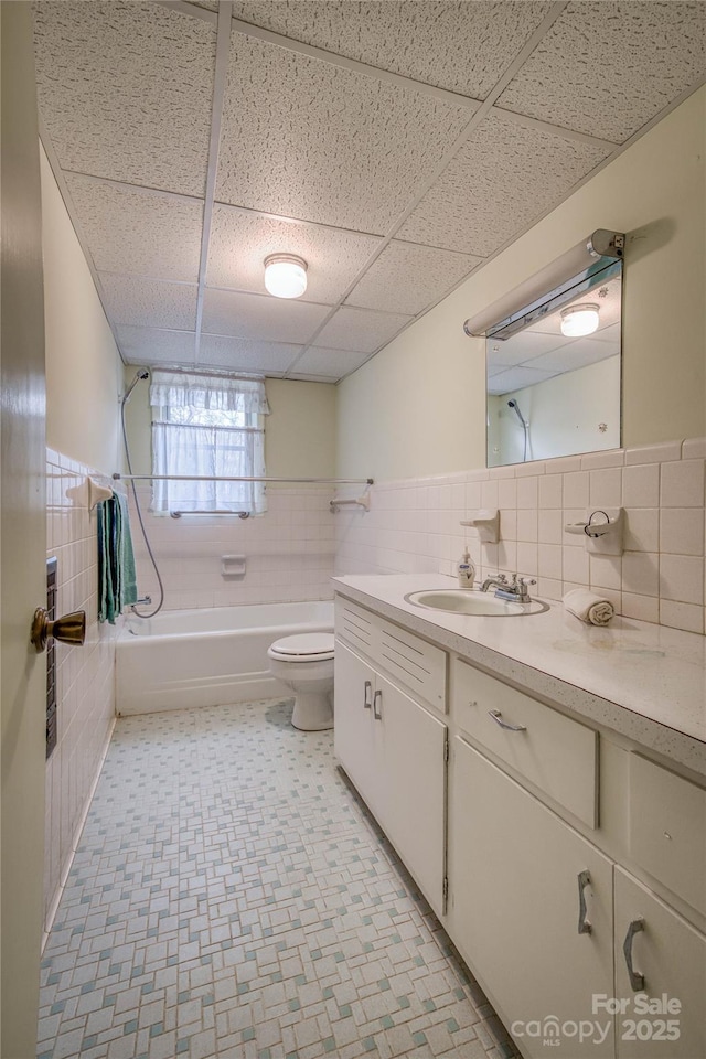 full bathroom with a drop ceiling, bathtub / shower combination, vanity, tile walls, and toilet