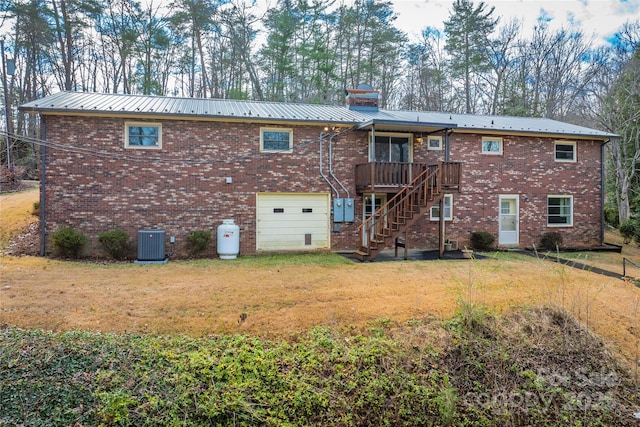 rear view of property featuring central AC unit, a garage, a wooden deck, and a lawn