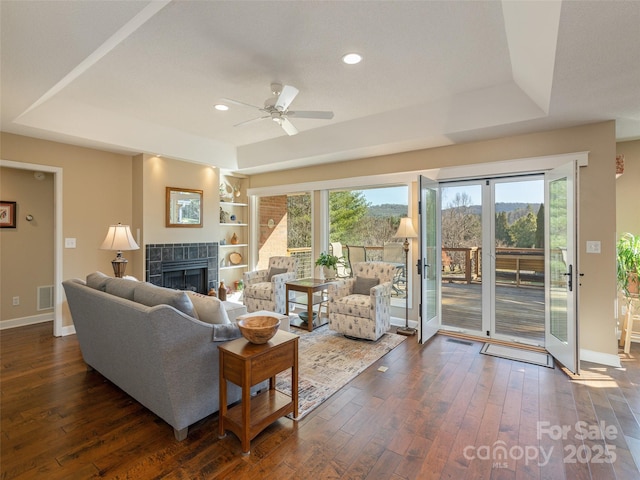 living room featuring ceiling fan, dark hardwood / wood-style floors, a raised ceiling, and a tiled fireplace