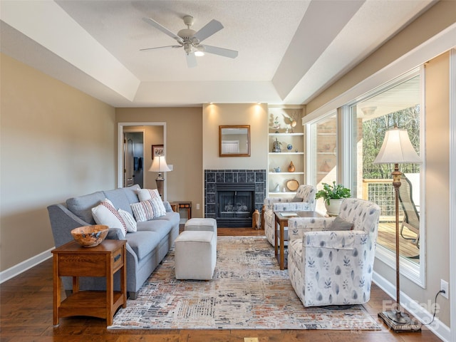 living room featuring a raised ceiling, ceiling fan, a tile fireplace, hardwood / wood-style flooring, and built in features