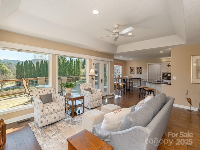 living room with french doors, a tray ceiling, ceiling fan, dark wood-type flooring, and sink