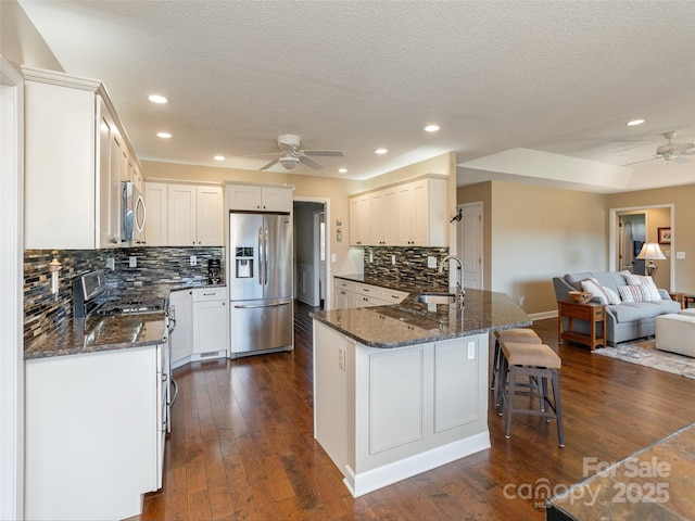 kitchen featuring ceiling fan, white cabinetry, stainless steel appliances, and dark stone counters