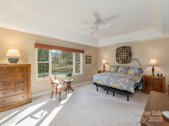 carpeted bedroom with a raised ceiling and ceiling fan