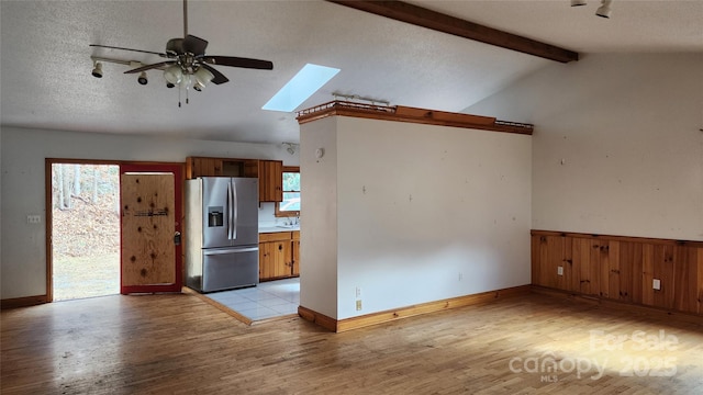 kitchen featuring light wood-type flooring, ceiling fan, lofted ceiling with skylight, and stainless steel refrigerator with ice dispenser