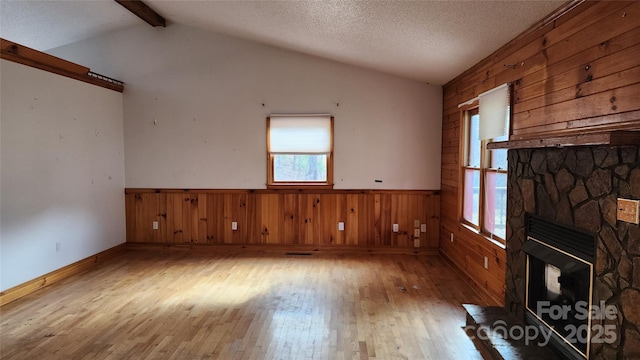 unfurnished living room with a fireplace, a textured ceiling, light hardwood / wood-style floors, and lofted ceiling with beams