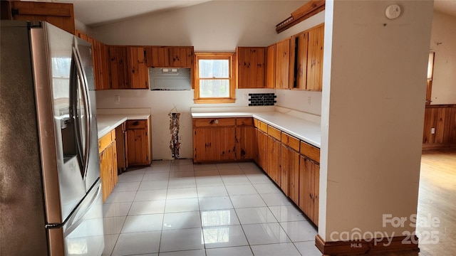 kitchen with stainless steel refrigerator with ice dispenser, light tile patterned flooring, and vaulted ceiling