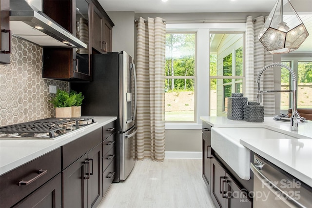 kitchen with appliances with stainless steel finishes, backsplash, wall chimney exhaust hood, dark brown cabinetry, and sink