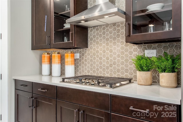 kitchen with dark brown cabinets, wall chimney range hood, and backsplash