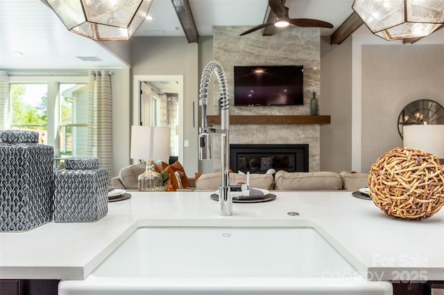 living room featuring ceiling fan, a fireplace, beamed ceiling, and sink