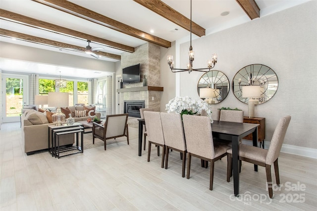 dining area featuring beamed ceiling, ceiling fan with notable chandelier, light hardwood / wood-style floors, and a tiled fireplace