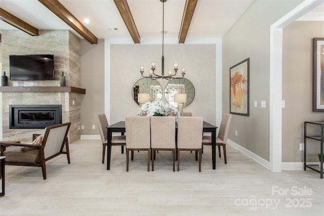 dining area featuring a fireplace, beamed ceiling, a chandelier, and light hardwood / wood-style floors