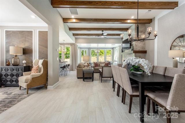 dining space with beamed ceiling, ceiling fan with notable chandelier, light hardwood / wood-style floors, and a stone fireplace