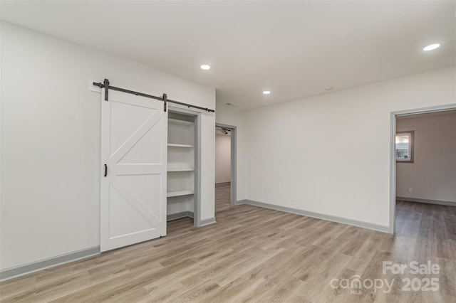 unfurnished bedroom with a barn door and light hardwood / wood-style floors