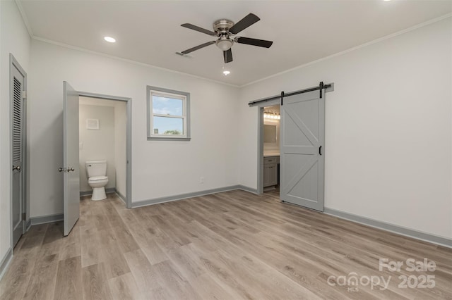 unfurnished bedroom with a barn door, ensuite bathroom, ceiling fan, and ornamental molding