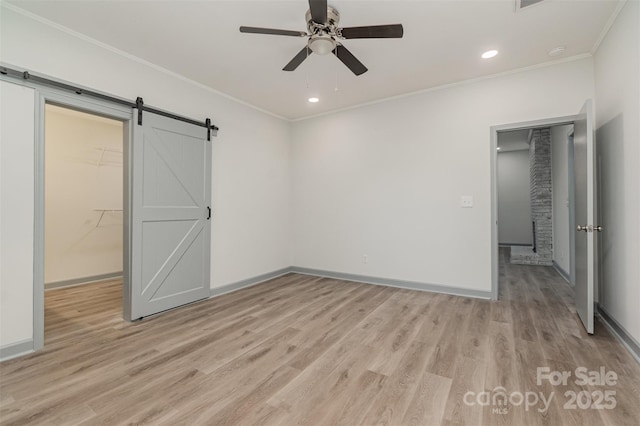 unfurnished bedroom with ceiling fan, a barn door, a walk in closet, a closet, and ornamental molding