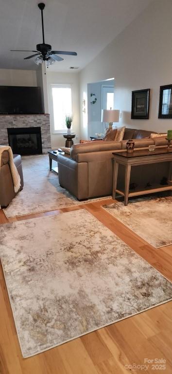 living room featuring hardwood / wood-style floors, ceiling fan, a stone fireplace, and vaulted ceiling