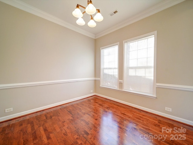 spare room featuring wood-type flooring, ornamental molding, and a notable chandelier