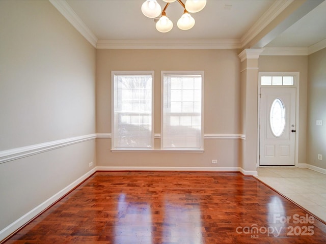 foyer entrance featuring ornate columns, hardwood / wood-style flooring, an inviting chandelier, and ornamental molding