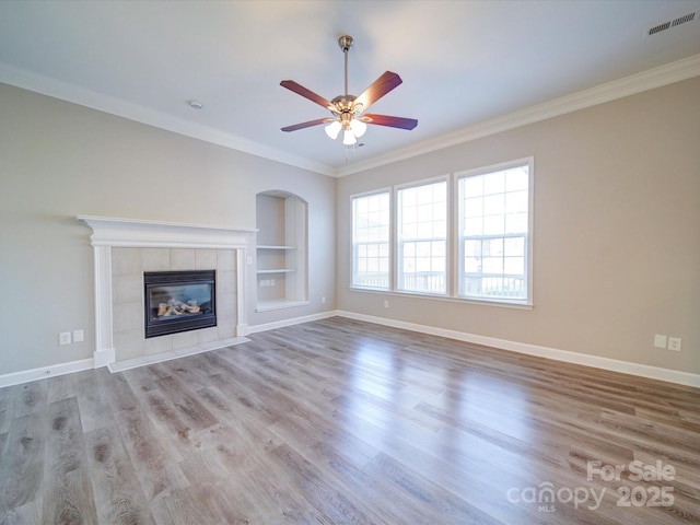 unfurnished living room with built in shelves, a fireplace, ornamental molding, light wood-type flooring, and ceiling fan